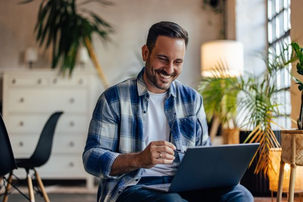 Casually dressed man smiling while using a laptop at home