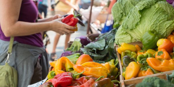 Colorful fresh produce at a farmers market with a woman holding a red bell pepper